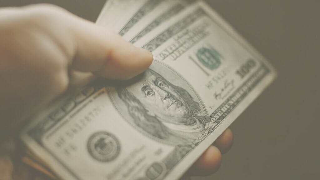 Imagem de uma mão segurando notas de dólar.